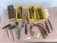 Overview of assorted tools including air ratchet wrench, T-handle wrenches, sockets, brass torch tips, clamp and drill bits displayed on carpet.