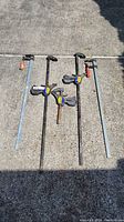 Four bar clamps laid on concrete surface, showing quick-release clamps and traditional clamp with red handle.