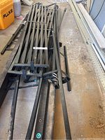 Black metal lattice panels and tubular rods for BBQ gazebo frame laid on ground.