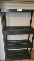 Front view of black plastic shelving unit showing four tiers and grid shelves.