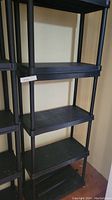 Full view of the black plastic shelving unit showing five shelves and four vertical support poles.