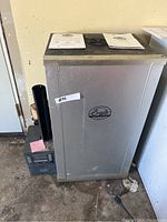 Front view of upright silver Bradley smoker with digital control unit mounted on side and instruction manuals on top