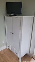 Full view of white Ikea armoire with TV on top, showing the two doors and three drawers at the bottom
