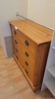 Front angled view of four drawer pine wood chest of drawers with round metal ring pull handles, showing natural wood grain and light wear.