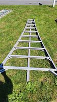 Curved aluminum ladder section with flat rectangular rungs and integrated hooks, lying on grass