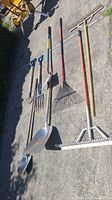 View of all landscaping tools laid out on pavement including shovels, rakes, pitchfork, edger, and hoe.