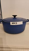 Blue Le Creuset Dutch oven front view with lid and label #143 on exterior.