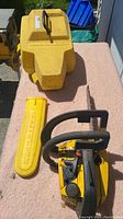 McCulloch chainsaw unit, yellow plastic protective case, and yellow plastic bar cover displayed on pink surface outdoors.