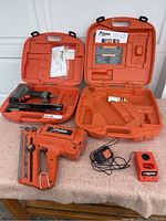 Two orange cases, cordless framing nailer, pneumatic finishing nailer, charger, and instruction manuals shown on table.