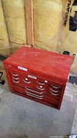 Full front view of red metal tool box with drawers, showing wear and a label.