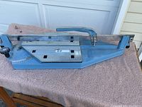 Front angle view of the blue Sigma tile cutter on a table with measuring ruler and cutting handle visible.