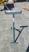 Full view of the green steel roller saw stand with cylindrical roller and adjustable height feature.