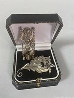 Ornate brooch with blue stones and floral leaf design brooch displayed in black and white presentation box.