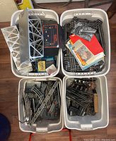 Four plastic bins filled with scale train tracks, wiring, a metal bridge, control panels, and documentation. The items show signs of use and wear.