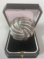Front view of sterling silver brooch in black jewelry box showing ribbed swirl design