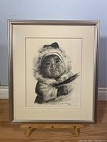Framed print showing full view of artwork featuring Inuit baby in warm clothing with fur hood, signature visible.