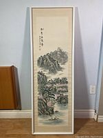 Full view of framed painting showing traditional Chinese landscape with mountains, water, trees, boat, in vertical narrow white frame.