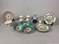 Overview of lot showing decorative plates, candleholders, miniature phonograph, and other porcelain pieces arranged on table.