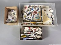 Three containers of assorted vintage circulated postage stamps, mostly loose and attached to pieces of envelopes, displayed from above.