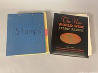 Two stamp albums, one blue labeled 'Stamps', the other black titled 'The New World Wide Stamp Album'