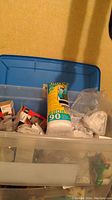 Photo of storage bin lid and variety of light bulb boxes, vent filter tube, and other items inside the bin.
