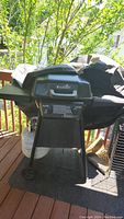 Side view showing grill on stand with wheels, propane tank connected, and black cover partially on.