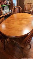 Top view of round wooden dining table with extension leaf and surrounding chairs.