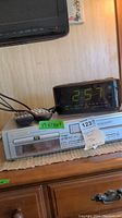 Emerson VHS/DVD combo player with remote control on top, placed underneath GE clock radio on wooden surface