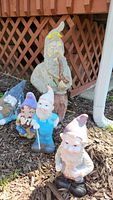 Photo of five garden gnomes including one large cement gnome and four smaller plastic and ceramic gnomes arranged outside.