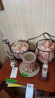 Side view of the lot showing three Himalayan salt lamps with pink salt chunks in wire baskets, the Galileo thermometer, storm glass, and a small decorative item with a lattice design.