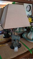 Front view of the lamp showing the stag base and fabric shade on a wooden surface against a mirror background.