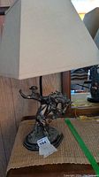Full view of the cowboy riding horse lamp with shade on, showing the detailed resin and metal base and beige shade.