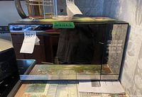 Closed microwave oven showing mirrored black glass door with numeric control panel on right side and external dimension label on top.