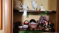 Shelf display featuring multiple milk glass items on the upper shelf, Americana-themed ceramics and figurines on the lower shelf, showing patriotic colors and various kitchenware pieces.