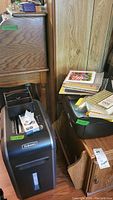 Fellowes paper shredder next to a wood table and black storage tub with photo albums and notebooks