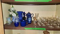 Shelf display showing a variety of etched crystal stemware including cordial, champagne, and wine glasses along with vases and other items.