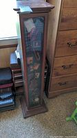 Full view of tall wooden tape cabinet with glass front showing tapes and decorative items inside.