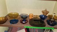 Wide view showing a collection of various vintage glass pieces including amber, cobalt, ruby, and iridescent colors displayed on shelving.