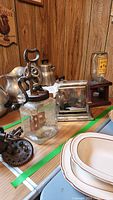 Photo showing vintage kitchen items on table: glass churn with iron grinder, stainless steel toaster, candy jar, and other vintage kitchenware
