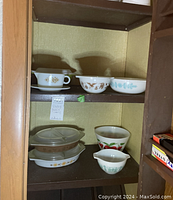 Shelf display with three bowls on top shelf and four bowls/dishes on bottom shelf, showcasing different vintage Pyrex patterns and designs.
