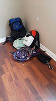 Photo of four backpacks including a blue and black Serratus backpack, white and orange hard-back backpack, purple floral backpack, and mint green soft backpack.