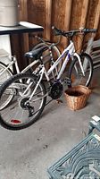 Side view of a white Supercycle 1800 bicycle with knobby tires and a wicker basket placed near the rear wheel, in a garage setting.
