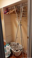 Coat rack, laundry basket with items, and wooden hangers on closet hanging rod