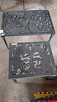 Photo showing top view of two black iron garden tables with ornate scrollwork design, one rectangular and one square.
