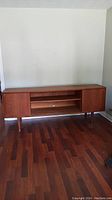 Front view of teak credenza showing sliding doors, center open shelving and legs