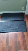 Two black rubber mats with sloped angle edges placed on wooden floor near wall and outlet.