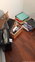 Photo showing Casemate paper shredder next to wicker basket filled with pencils, pens, markers, next to a black Asus keyboard and stacked notebooks and folders.