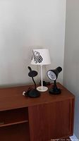 Three table lamps on wooden cabinet; two black goose neck lamps and one white side table lamp with owl shade.