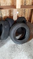Four black BFGoodrich tires stacked in a wooden shed with concrete floor.