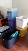 Stack of various plastic storage totes in multiple colors and sizes on hardwood floor